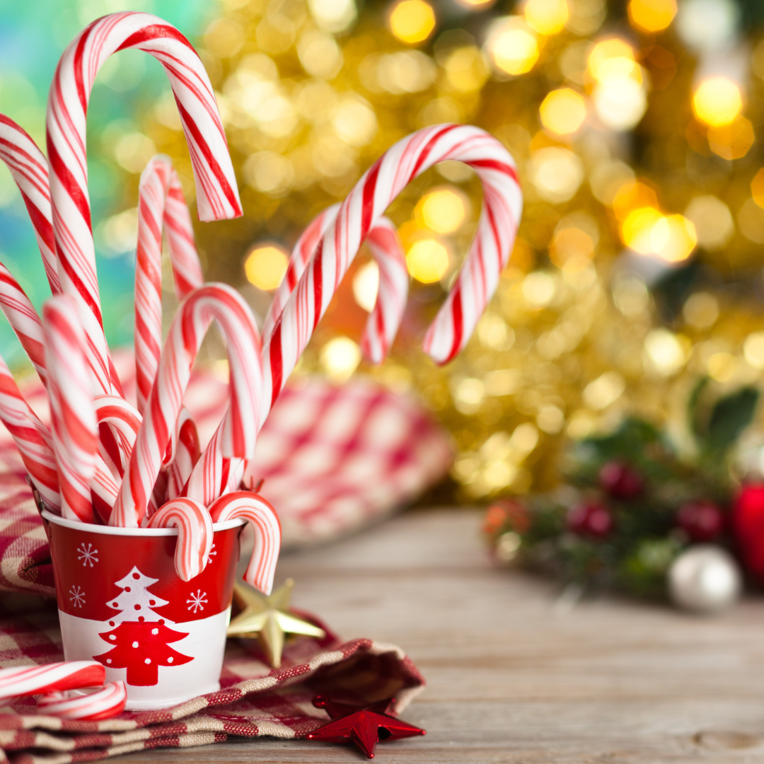 Red & White striped candy canes in red & white paper cup decorated with a christmas tree. Positioned on a table with a blurred gold christmas tree in the background.